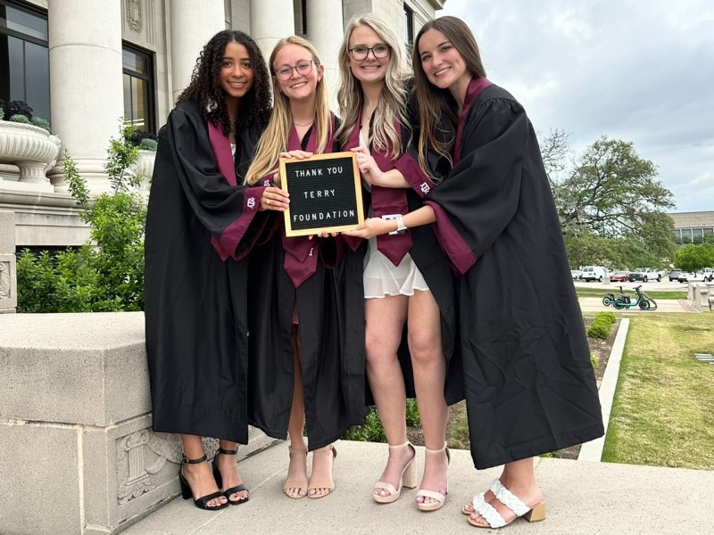 four women in black graduation gowns holding a sign that says "Thank You Terry Foundation"