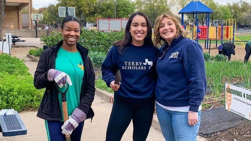 Three women pausing to smile at the camera while working in a garden for a service project.